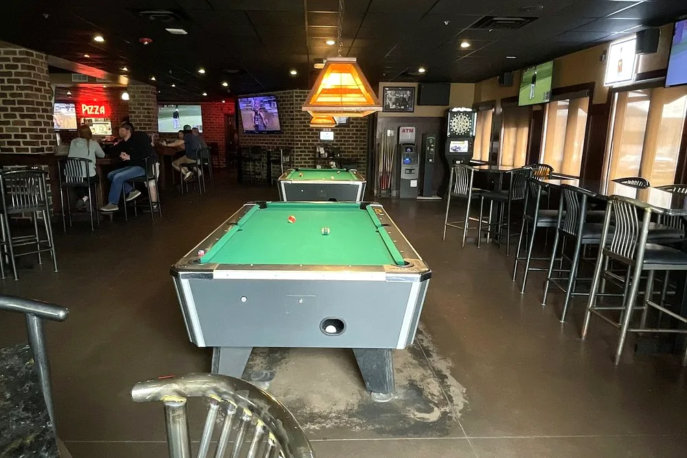 The pool table and bar stools inside the 18th Amendment, with booths and TVs along the brick wall behind
